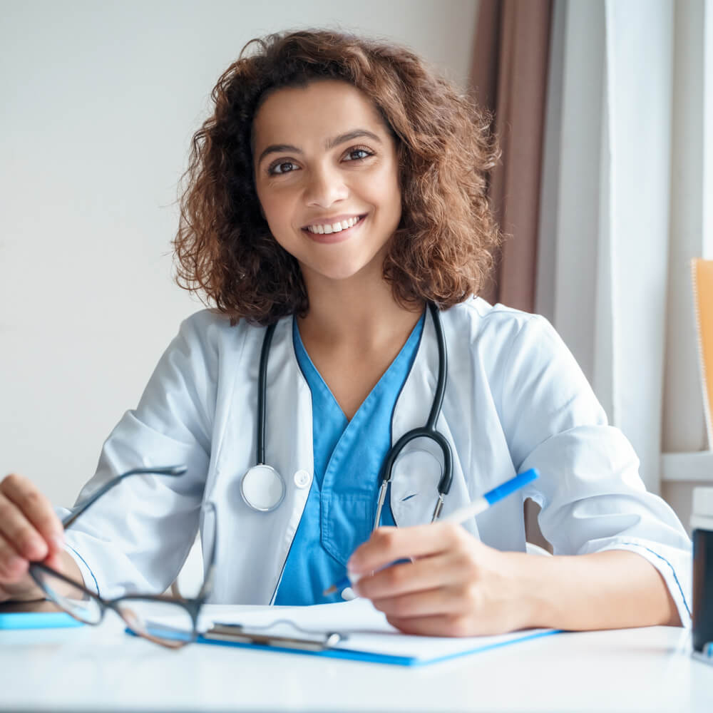 female doctor sitting on work desk and smiling at camera